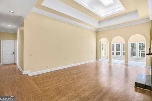 unfurnished living room featuring a skylight, wood-type flooring, ornamental molding, and a raised ceiling