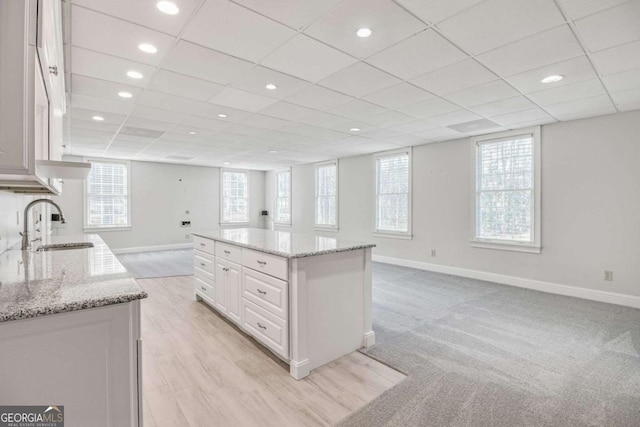 kitchen with a kitchen island, sink, white cabinets, and light stone counters