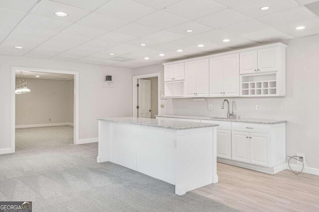 kitchen featuring sink, white cabinetry, a center island, light stone countertops, and a drop ceiling