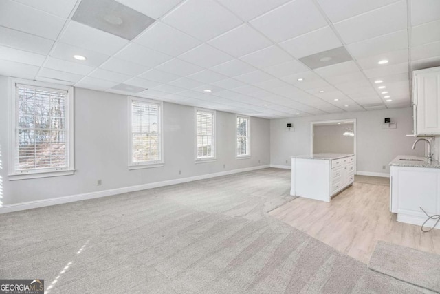 unfurnished living room with a paneled ceiling, sink, and light carpet