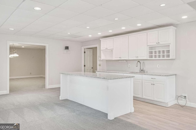 kitchen with sink, light stone countertops, light hardwood / wood-style floors, white cabinets, and a kitchen island