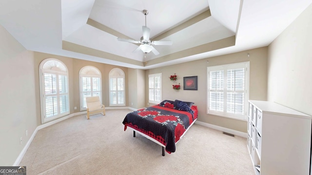 bedroom with a raised ceiling, light colored carpet, and ceiling fan