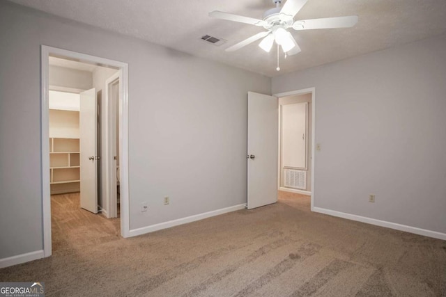 unfurnished bedroom featuring a spacious closet, light colored carpet, and ceiling fan