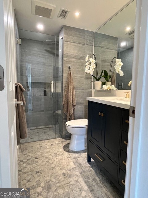 bathroom featuring vanity, toilet, a shower with shower door, and tile walls