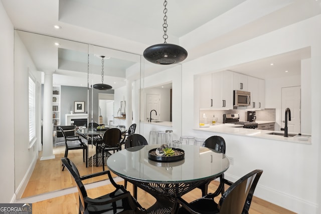 dining area featuring a tray ceiling, light wood-style floors, a fireplace, and baseboards