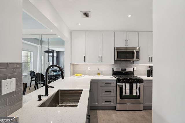 kitchen with appliances with stainless steel finishes, sink, gray cabinetry, decorative backsplash, and light stone counters