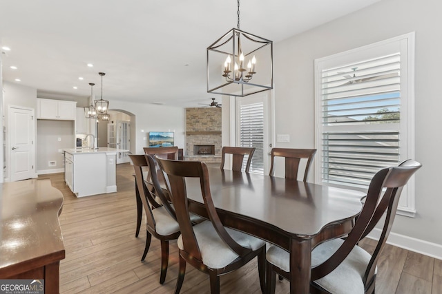 dining space with ceiling fan with notable chandelier, light wood-type flooring, sink, and a fireplace