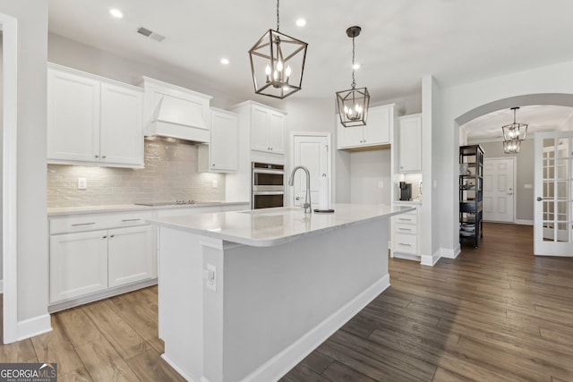 kitchen featuring white cabinetry, a kitchen island with sink, pendant lighting, and premium range hood