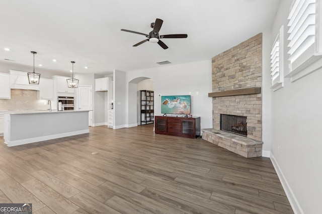 unfurnished living room with hardwood / wood-style flooring, a stone fireplace, and ceiling fan with notable chandelier