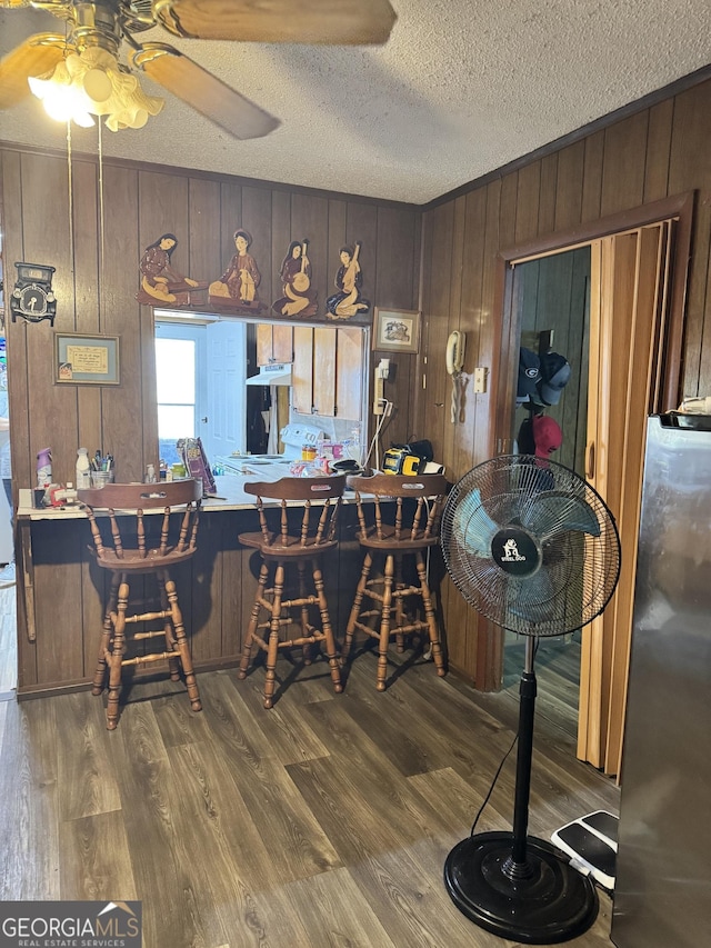 dining area with ceiling fan, hardwood / wood-style flooring, a textured ceiling, and wood walls