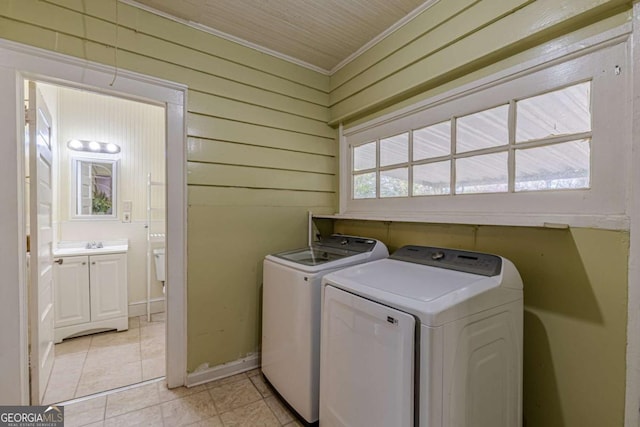 clothes washing area with light tile patterned flooring, sink, wood walls, washer and dryer, and ornamental molding