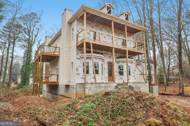 back of house featuring a chimney and a balcony