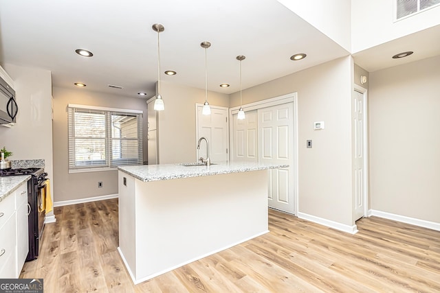 kitchen with sink, light stone counters, black appliances, a center island with sink, and decorative light fixtures