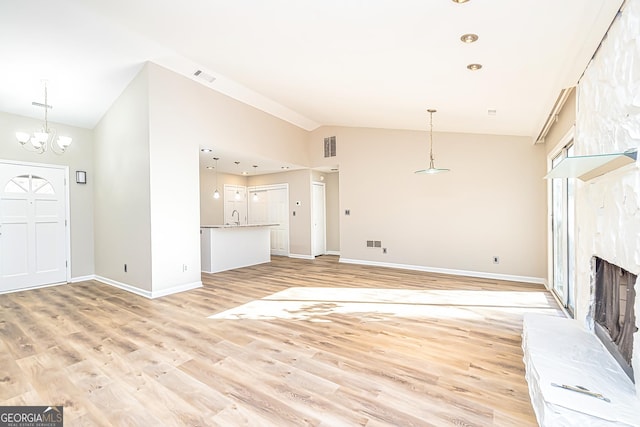 unfurnished living room featuring sink, an inviting chandelier, high vaulted ceiling, light wood-type flooring, and a fireplace