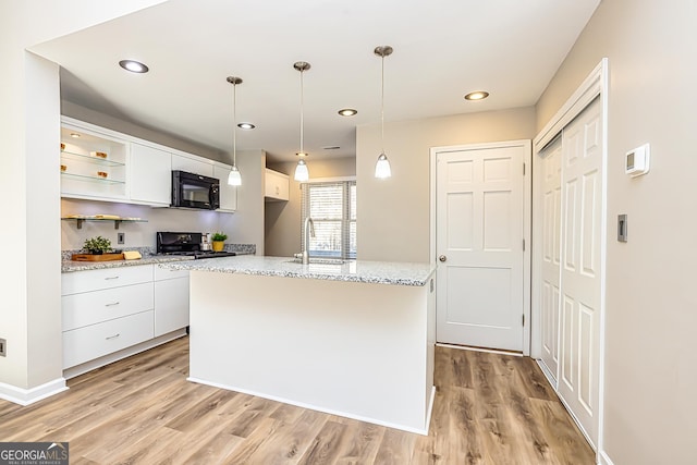 kitchen with sink, range, an island with sink, white cabinets, and decorative light fixtures