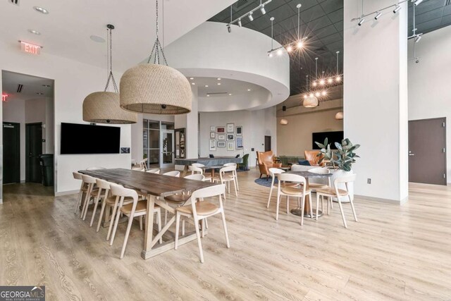 dining area featuring rail lighting, light hardwood / wood-style flooring, and a high ceiling