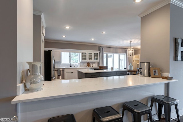 kitchen with a breakfast bar, plenty of natural light, kitchen peninsula, stainless steel appliances, and white cabinets