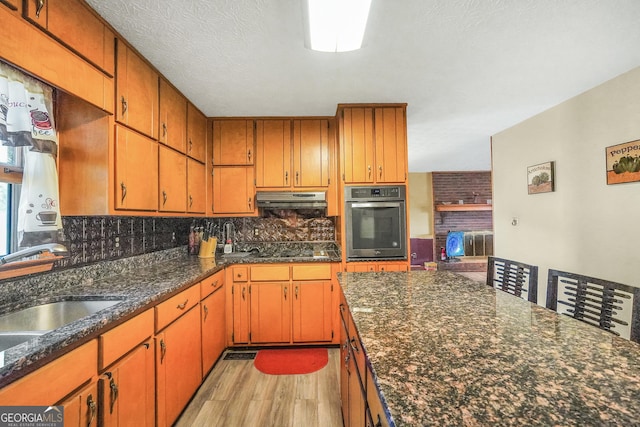 kitchen with light wood-type flooring, wall oven, sink, and backsplash