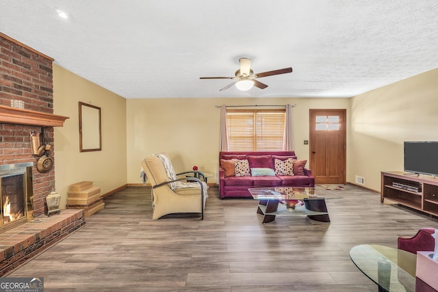 living room with hardwood / wood-style flooring, ceiling fan, a brick fireplace, and a textured ceiling