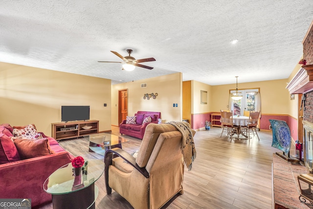 living room featuring ceiling fan, light hardwood / wood-style flooring, a textured ceiling, and a brick fireplace