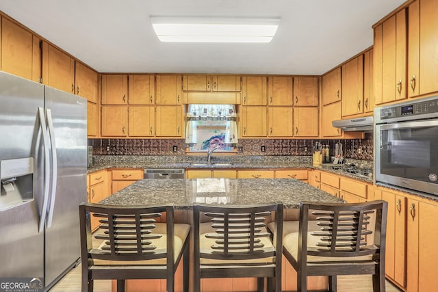 kitchen featuring sink, a center island, appliances with stainless steel finishes, a kitchen breakfast bar, and dark stone counters