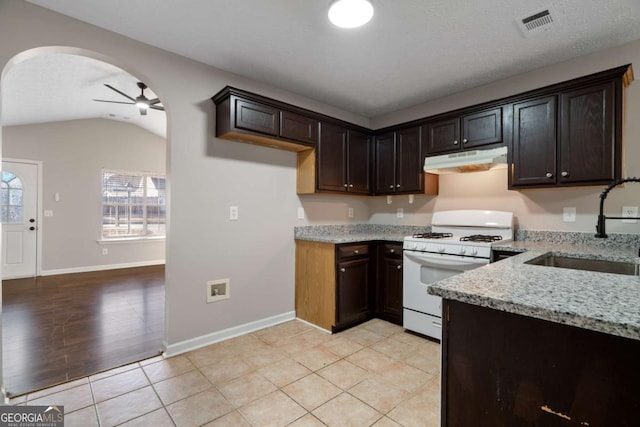 kitchen with sink, white gas range oven, ceiling fan, dark brown cabinets, and light stone counters