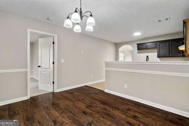 unfurnished dining area featuring a chandelier, dark hardwood / wood-style floors, sink, and a textured ceiling