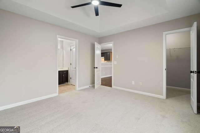 unfurnished bedroom featuring connected bathroom, a spacious closet, ceiling fan, light carpet, and a closet