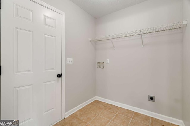 clothes washing area with electric dryer hookup, light tile patterned floors, and a textured ceiling