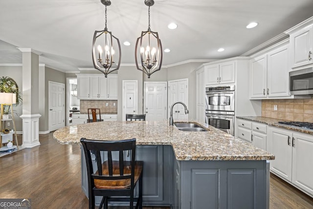 kitchen featuring sink, white cabinetry, appliances with stainless steel finishes, pendant lighting, and a kitchen island with sink