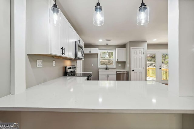 kitchen with appliances with stainless steel finishes, decorative light fixtures, a wealth of natural light, and white cabinets