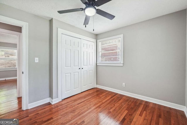 unfurnished bedroom featuring hardwood / wood-style flooring, ceiling fan, multiple windows, and a closet