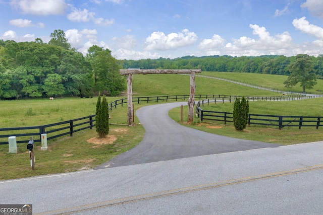 view of community featuring a lawn, a rural view, fence, and aphalt driveway