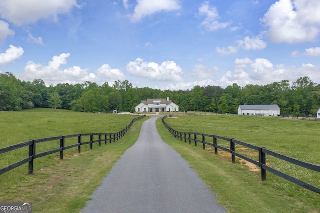 view of road with a rural view, a wooded view, and aphalt driveway