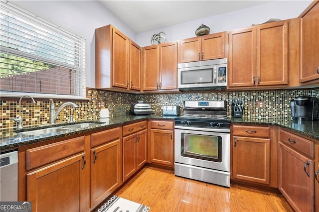 kitchen featuring sink, light hardwood / wood-style flooring, dark stone counters, and appliances with stainless steel finishes