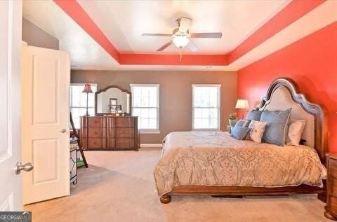 bedroom featuring light colored carpet, a raised ceiling, and ceiling fan