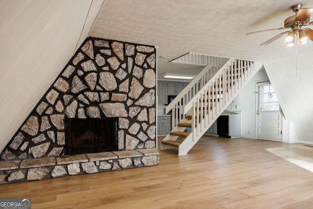 unfurnished living room featuring ceiling fan, a fireplace, hardwood / wood-style floors, and a textured ceiling