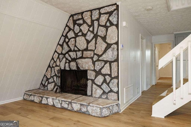 details with hardwood / wood-style flooring, a stone fireplace, wooden walls, and a textured ceiling