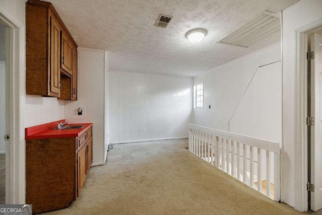 hallway with sink, light carpet, and a textured ceiling