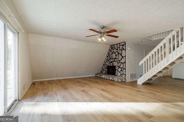 unfurnished living room with a fireplace, a textured ceiling, wood-type flooring, and ceiling fan