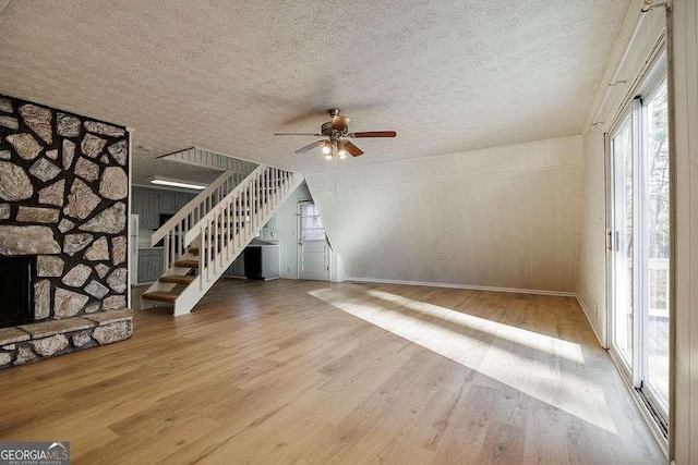 unfurnished living room with ceiling fan, hardwood / wood-style flooring, a stone fireplace, and a textured ceiling