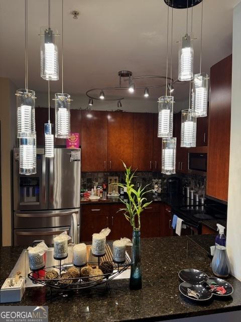 kitchen with hanging light fixtures, decorative backsplash, stainless steel refrigerator, and dark stone counters