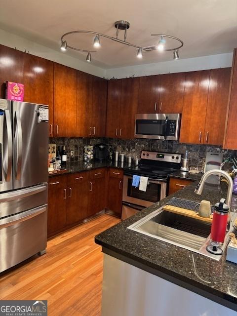 kitchen with sink, light wood-type flooring, appliances with stainless steel finishes, dark stone counters, and decorative backsplash