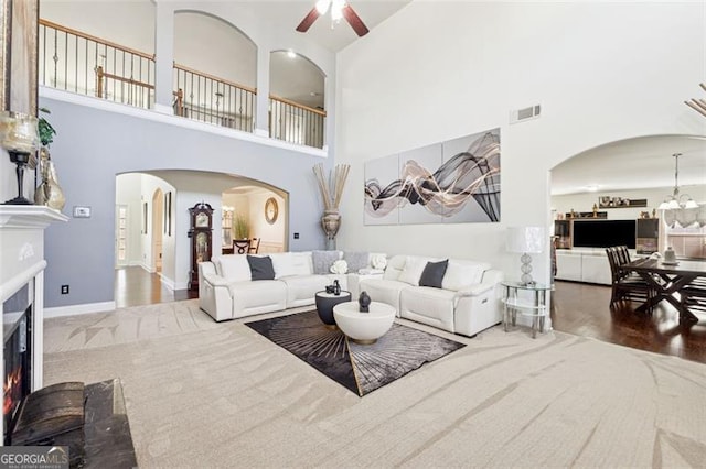 living room featuring a high ceiling, wood-type flooring, and ceiling fan with notable chandelier