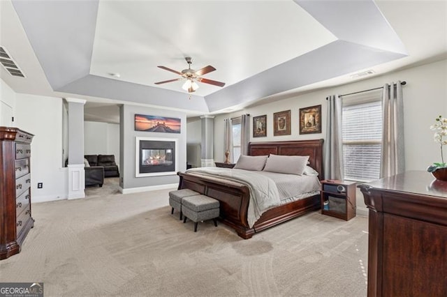 carpeted bedroom featuring multiple windows, ceiling fan, and a tray ceiling