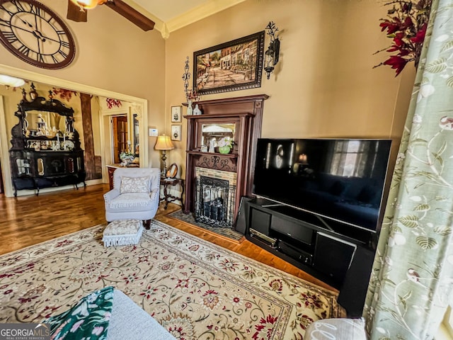 living room with crown molding, ceiling fan, wood-type flooring, and a high ceiling