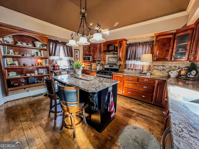 kitchen featuring wall chimney range hood, a breakfast bar area, appliances with stainless steel finishes, a center island, and decorative light fixtures