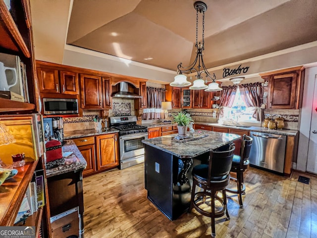 kitchen with a kitchen island, a kitchen bar, a tray ceiling, stainless steel appliances, and wall chimney exhaust hood