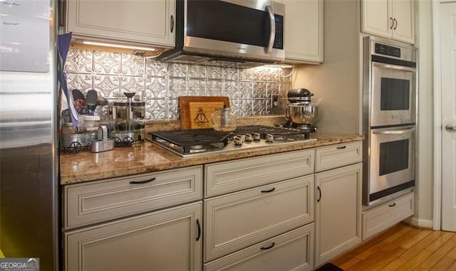 kitchen featuring appliances with stainless steel finishes, light stone countertops, decorative backsplash, and light hardwood / wood-style flooring