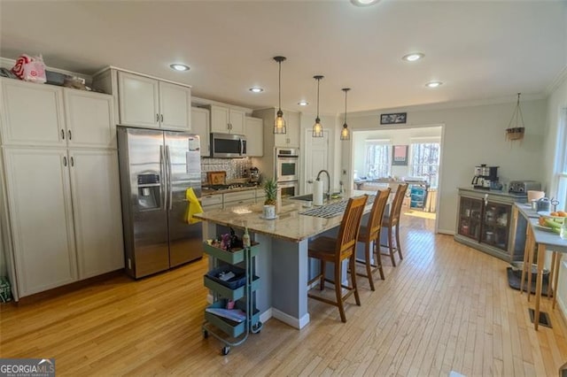 kitchen with white cabinetry, hanging light fixtures, stainless steel appliances, light stone counters, and an island with sink